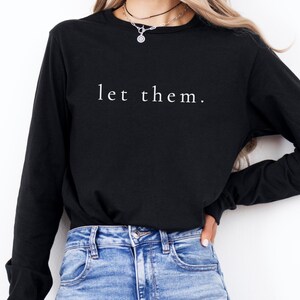 以下が含まれることがあります： 前面に白い文字で「let them.」がプリントされた黒い長袖シャツ