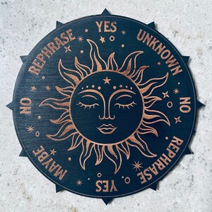 May include: A black wooden circular board with a gold sun design and the words "YES", "MAYBE", "NO", "REPHRASE", "UNKNOWN", and "REPHRASE" around the edge.