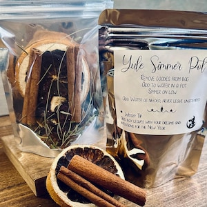 May include: Two clear pouches and a silver pouch containing ingredients for a Yule Simmer Pot. The pouches contain dried orange slices, cinnamon sticks, and herbs. The silver pouch has text that reads "Yule Simmer Pot".