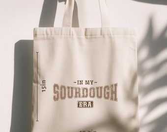 May include: Cream-colored tote bag with the text "-IN MY- SOURDOUGH ERA" in brown lettering. The bag is 15 inches tall and 17.7 inches wide, with two cream-colored handles.