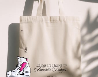 Könnte beinhalten: Cremefarbene Tragetasche mit dem Text "Things are a few of my Favorite Things". Eine Rollschuhgrafik mit einem rosa Blitz befindet sich links. Die Tasche ist 38 cm hoch und 45 cm breit.
