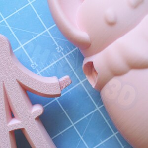 Op de afbeelding: Close-up van een lichtroze 3D-geprint object, mogelijk een onderdeel van een groter ontwerp. Het object is geplaatst op een blauwe snijmat met meetmarkeringen. Het nummer "30" is vaag zichtbaar op het object.