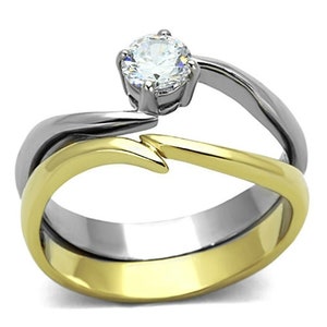 Peut inclure: Une bague bicolore or et argent avec une seule pierre ronde transparente au centre. La bague a un design unique avec une bande incurvée.