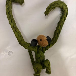 May include: A handmade green braided rope monkey with a walnut head and black ears. The monkey's arms form a heart shape. The monkey is a unique decorative item.