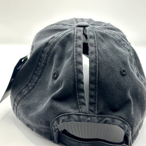 K&ouml;nnte beinhalten: Schwarze Baseballkappe aus Baumwolle mit einer &Ouml;ffnung hinten und einem schwarzen verstellbaren Riemen.