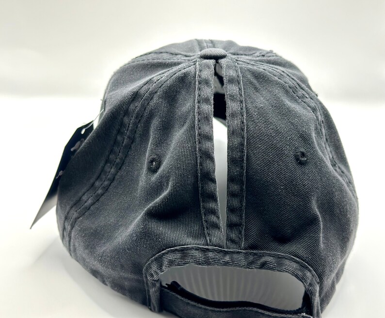 K&ouml;nnte beinhalten: Schwarze Baseballkappe aus Baumwolle mit einer &Ouml;ffnung hinten und einem schwarzen verstellbaren Riemen.