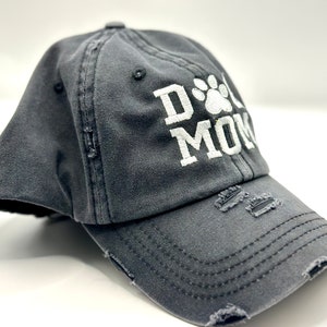 K&ouml;nnte beinhalten: Eine graue, abgenutzte Baseballkappe mit wei&szlig;er Stickerei, auf der "Dog Mom" mit einem Pfotenabdruck steht.