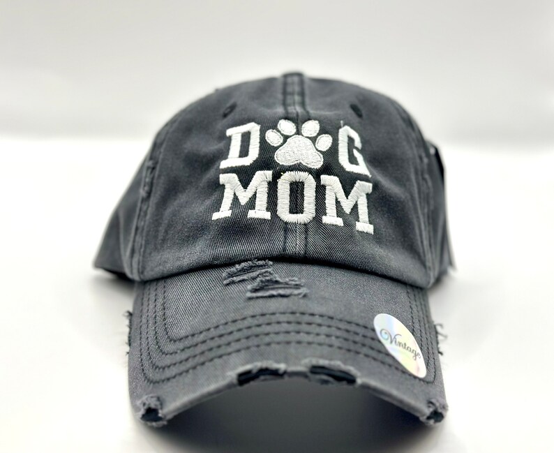 K&ouml;nnte beinhalten: Eine graue, abgenutzte Baseballkappe mit einem wei&szlig;en gestickten Pfotenabdruck und dem Text "DOG MOM".