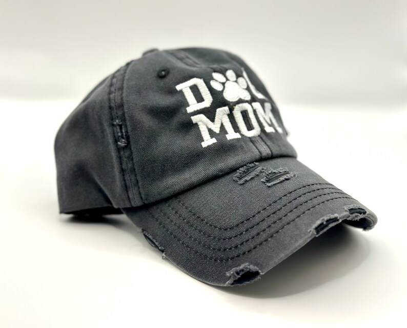 K&ouml;nnte beinhalten: Eine schwarze, abgenutzte Baseballkappe mit einem wei&szlig;en gestickten Pfotenabdruck und dem Text "Dog Mom".