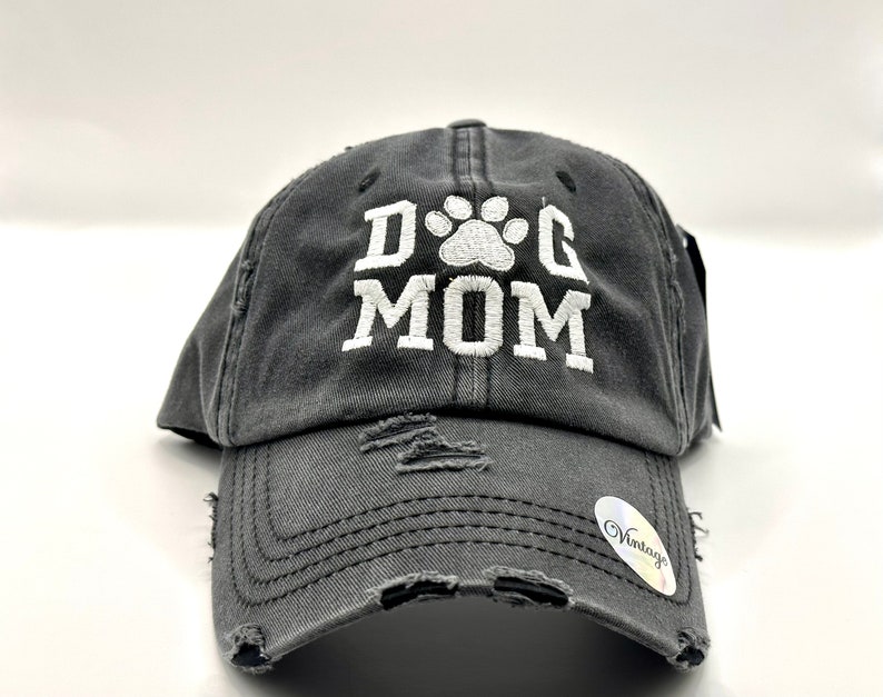 K&ouml;nnte beinhalten: Eine graue, abgenutzte Baseballkappe mit einem wei&szlig;en gestickten Pfotenabdruck und dem Text "DOG MOM".