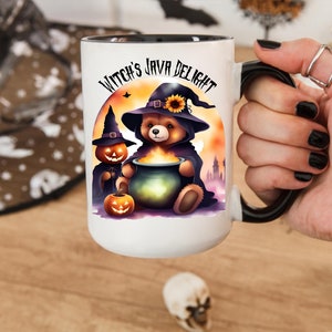 May include: White ceramic mug with a black handle. The mug features a cartoon illustration of a bear wearing a witch's hat and holding a cauldron. The text "Witch's Java Delight" is printed on the mug.