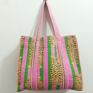 Könnte beinhalten: Rosa und grün gestreifte Tragetasche mit Tigerdruck. Die Tasche hat vertikale Streifen in Rosa und Grün mit Tigerillustrationen. Die Griffe und Kanten sind mit einem rot-weißen Muster verziert. Die Tasche hängt an einer weißen Wand.