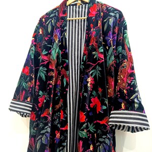 Puede incluir: Un kimono de terciopelo negro con estampado floral que presenta p&aacute;jaros, flores y hojas. El kimono tiene un forro a rayas y pu&ntilde;os a rayas.