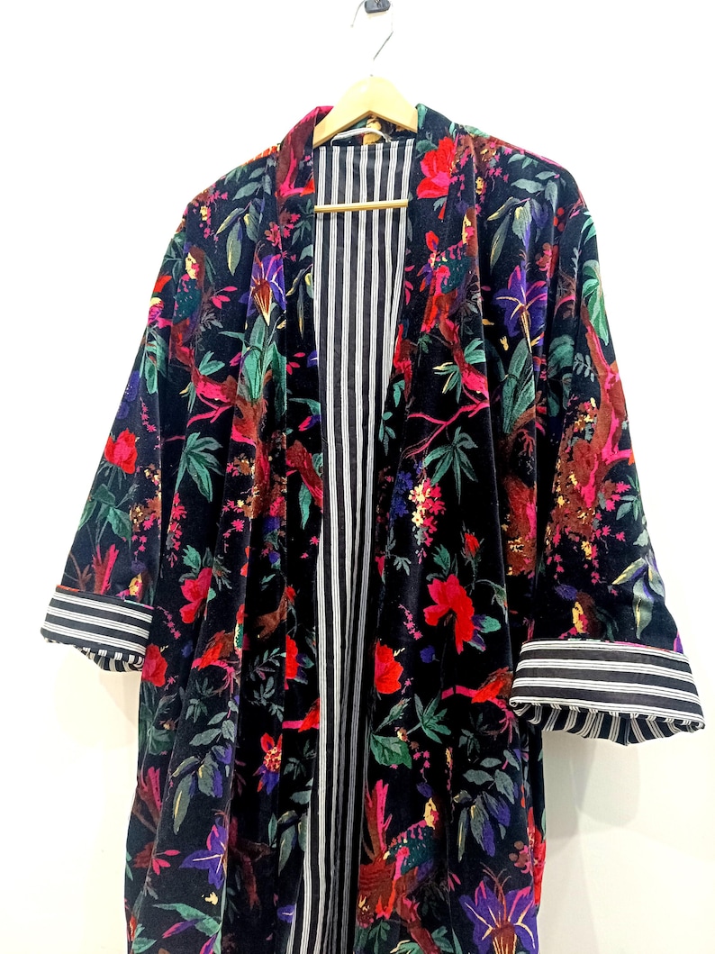 Puede incluir: Un kimono de terciopelo negro con estampado floral que presenta p&aacute;jaros, flores y hojas. El kimono tiene un forro a rayas y pu&ntilde;os a rayas.