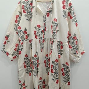 May include: A white cotton dress with a floral print in shades of red and green. The dress has a V-neckline and 3/4 sleeves.