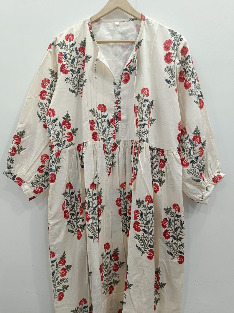 May include: A white cotton dress with a floral print in shades of red and green. The dress has a V-neckline and 3/4 sleeves.