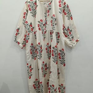 May include: A white cotton dress with a floral print in shades of red and green. The dress has a round neckline and 3/4 sleeves.