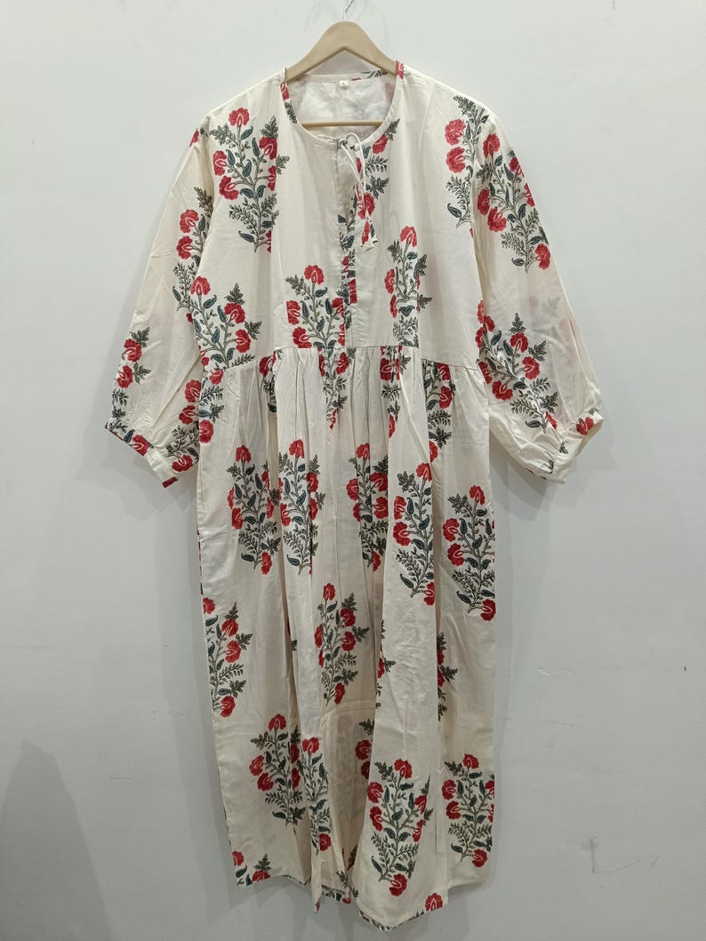 May include: A white cotton dress with a floral print in shades of red and green. The dress has a round neckline and 3/4 sleeves.