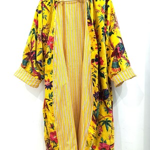 Puede incluir: Un kimono amarillo con estampado floral y de p&aacute;jaros. El kimono tiene un forro a rayas y est&aacute; abierto por delante.