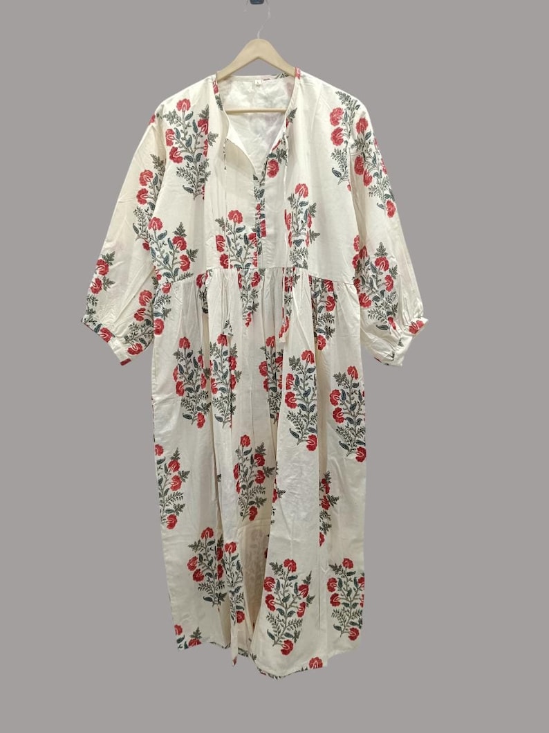 May include: A white cotton dress with a floral print in shades of red and green. The dress has a V-neckline, 3/4 sleeves, and a gathered skirt.