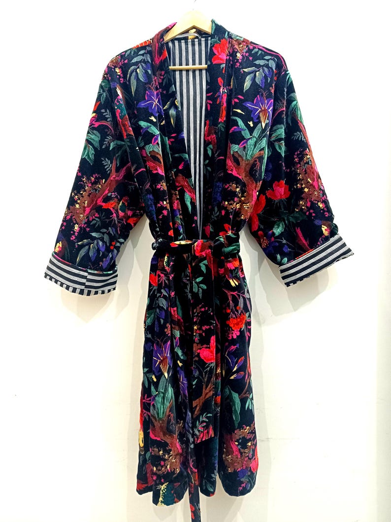 Puede incluir: Una bata de terciopelo negro con estampado floral de colores. La bata tiene un cintur&oacute;n a juego y ribetes a rayas en las mangas.