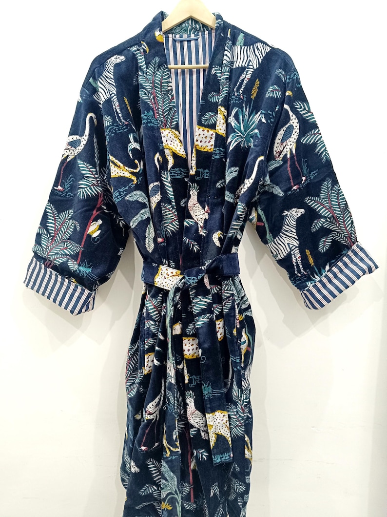 Puede incluir: Una bata de terciopelo azul marino con estampado de animales de colores que incluye cebras, leopardos y p&aacute;jaros. La bata tiene un cintur&oacute;n a juego y un forro a rayas.