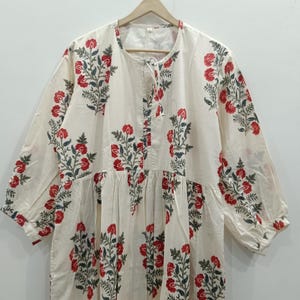 May include: A white cotton dress with a floral print in shades of red and green. The dress has a round neckline and three-quarter sleeves.