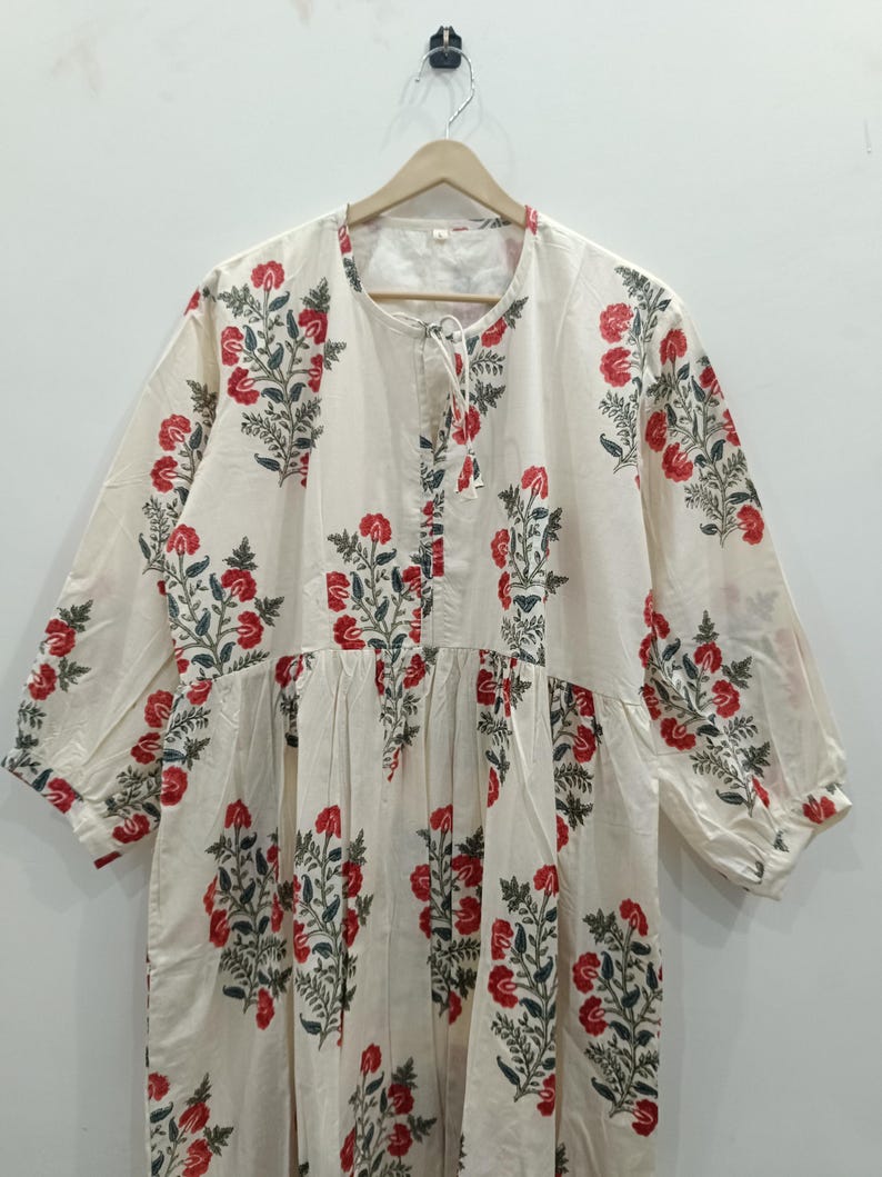 May include: A white cotton dress with a floral print in shades of red and green. The dress has a round neckline and three-quarter sleeves.