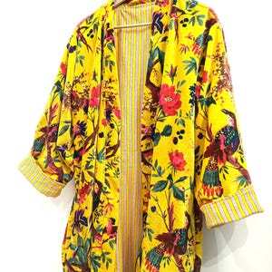 Puede incluir: Un kimono amarillo con estampado floral con p&aacute;jaros y flores. El kimono tiene un forro a rayas y est&aacute; hecho de una tela suave y ligera.