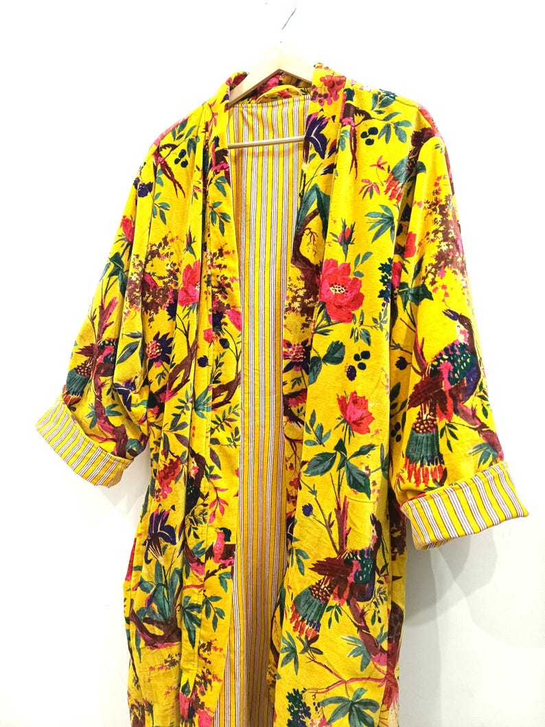 Puede incluir: Un kimono amarillo con estampado floral con p&aacute;jaros y flores. El kimono tiene un forro a rayas y est&aacute; hecho de una tela suave y ligera.
