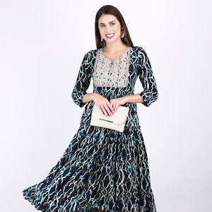 May include: A blue and white patterned dress with a tiered skirt and embroidered neckline. The dress has a 3/4 sleeve and is worn with a white clutch and green heels.