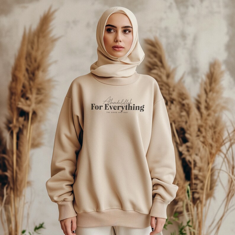 May include: A beige sweatshirt with the text "Alhamdulillah For Everything The Good And The Bad" printed on the front. The model is wearing a beige headscarf.