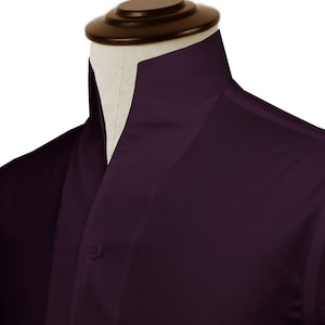 May include: A close-up of a dark purple dress shirt with a mandarin collar. The shirt is buttoned at the top and is displayed on a mannequin. The fabric appears smooth and has a slight sheen.