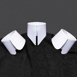 以下が含まれることがあります： 3つの白い取り外し可能な襟が、それぞれ鮮明な折り畳みデザインで、暗く質感のある生地の上に展示されています。 襟は、どのように着用されるかを示唆するように配置されており、そのクリーンなラインとクラシックなスタイルを強調しています。