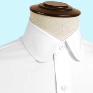 May include: A white dress shirt with a rounded collar and button-down front. The shirt is displayed on a mannequin head with a brown top. The collar is a prominent feature, and the shirt appears to be made of a crisp, smooth fabric.