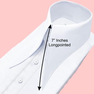 May include: Close-up of a crisp white dress shirt with a long-pointed collar. The collar measures 7 inches. The shirt has three visible buttons and is neatly folded. The background is a soft pink.