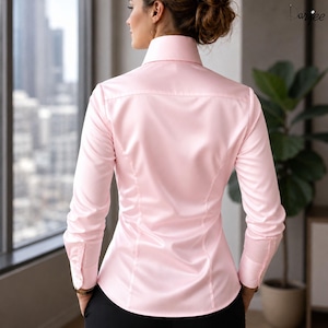 May include: A light pink long-sleeve button-down shirt with a classic collar. The shirt has a tailored fit and is made of a smooth, possibly satin-like fabric. The cuffs are buttoned, and the back of the shirt is visible.
