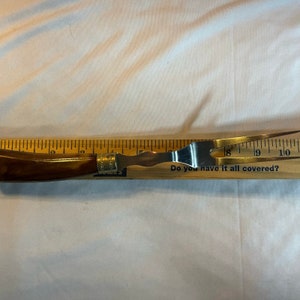 May include: A brown wooden handled metal grilling fork with a measurement ruler in the background. The ruler reads "Do you have it all covered?"