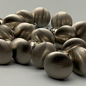 May include: A group of 15 silver cabinet knobs with a smooth, rounded surface. The knobs are arranged in a pile, with some overlapping.