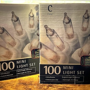 May include: Two boxes of clear mini light sets. Each box features 100 lights, with a lighted length of 24.8 ft and a total length of 27.1 ft. The boxes are labeled "Indoor/Outdoor" and "Connects End to End."