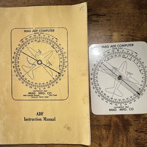 May include: A vintage Mag ADF Computer instruction manual with a tan cover and a matching white plastic flight computer tool. Both items feature a circular compass scale, an airplane graphic, and the text Mag ADF Computer, Copyright 1962.