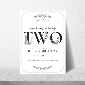 Op de afbeelding: Een witte uitnodigingskaart met een zwarte rand en bloemmotieven. De tekst luidt "hop on over some bunny is turning TWO" met een illustratie van een konijn en een eend. De uitnodiging is voor Julia's verjaardagsfeestje op zaterdag 25 juli om 11:00 uur. Het adres is No. 4 Calloway Drive.