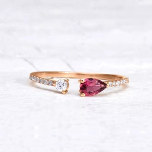 Peut inclure: Une délicate bague en or avec une pierre précieuse rose en forme de poire et une plus petite pierre ronde sertie dans une bande de diamants pavés.