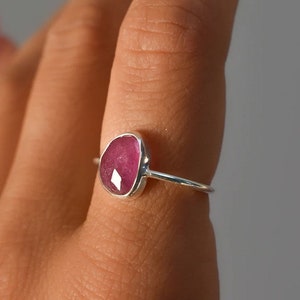 May include: A silver ring with a pink gemstone. The ring is on a finger.