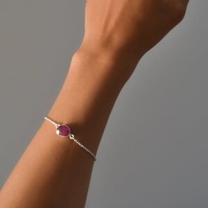 May include: A silver chain bracelet with a single oval-shaped ruby gemstone.