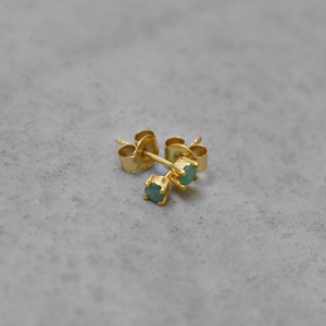 以下が含まれることがあります： 小さな丸い緑色の宝石が付いた、金のスタッドピアスのペアです。