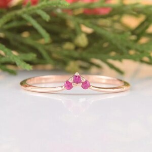 Op de afbeelding: Een delicate ring van roségoud met een kleine cluster van drie roze edelstenen in een chevron-vorm.