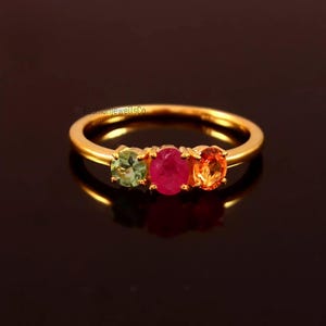 May include: A gold ring with three round gemstones. The gemstones are green, red, and orange.