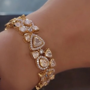 May include: A gold bracelet with a row of large, clear, faceted gemstones set in a gold frame. The bracelet is on a person's wrist.
