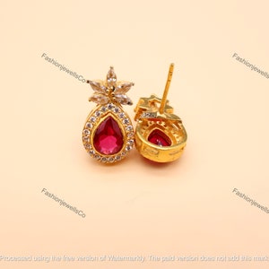 Puede incluir: Un par de pendientes de oro con una piedra roja en forma de lágrima rodeada de piedras de circonita cúbica transparentes. Los pendientes tienen un diseño en forma de flor en la parte superior y un sello 925 en la parte posterior.